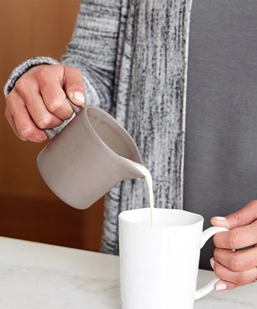 Woman pouring milk into coffee mug